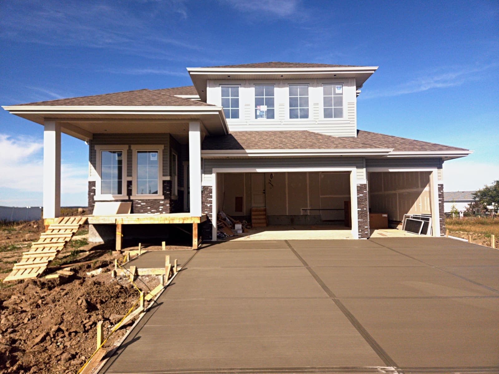 Front of the Olivia in Tofield, a two-storey home with a covered veranda, ledgestone accents and a triple attached garage
