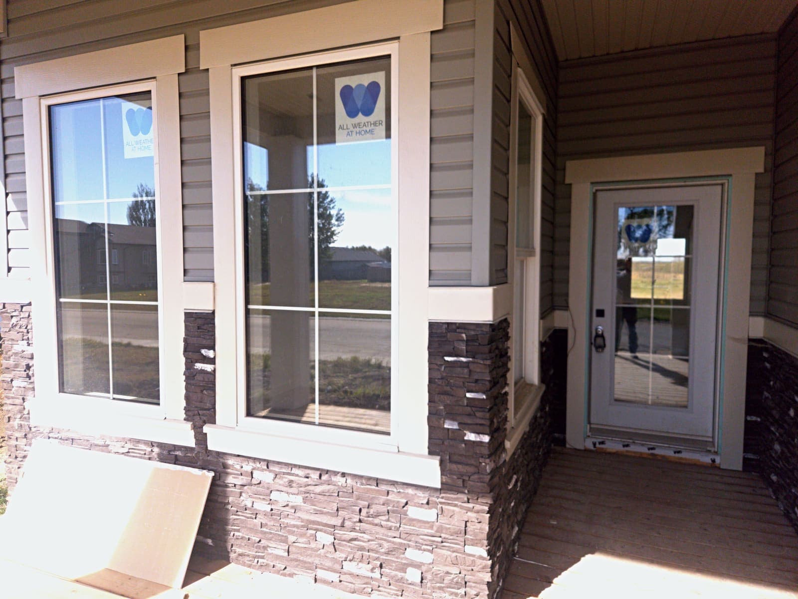 Front entry with a full-lite door, colonial grille windows and ledgestone wainscot under the veranda