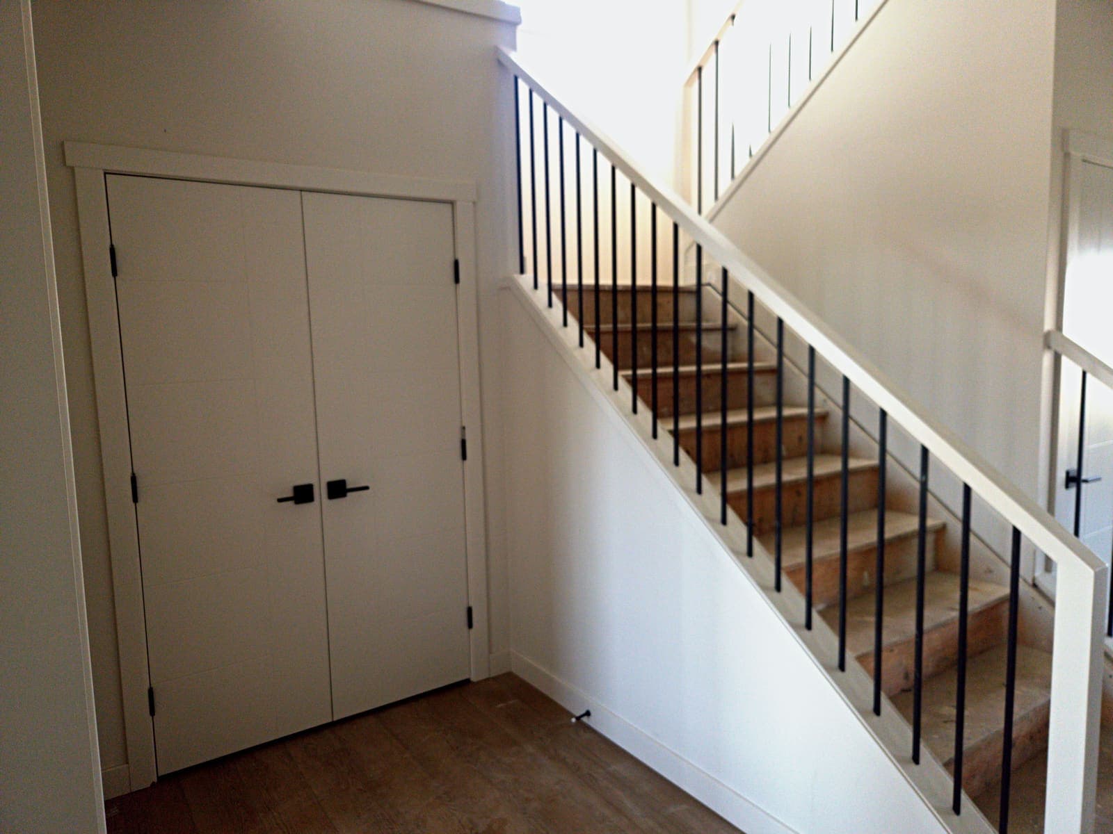 Front closet double doors beside the staircase with matte black balusters