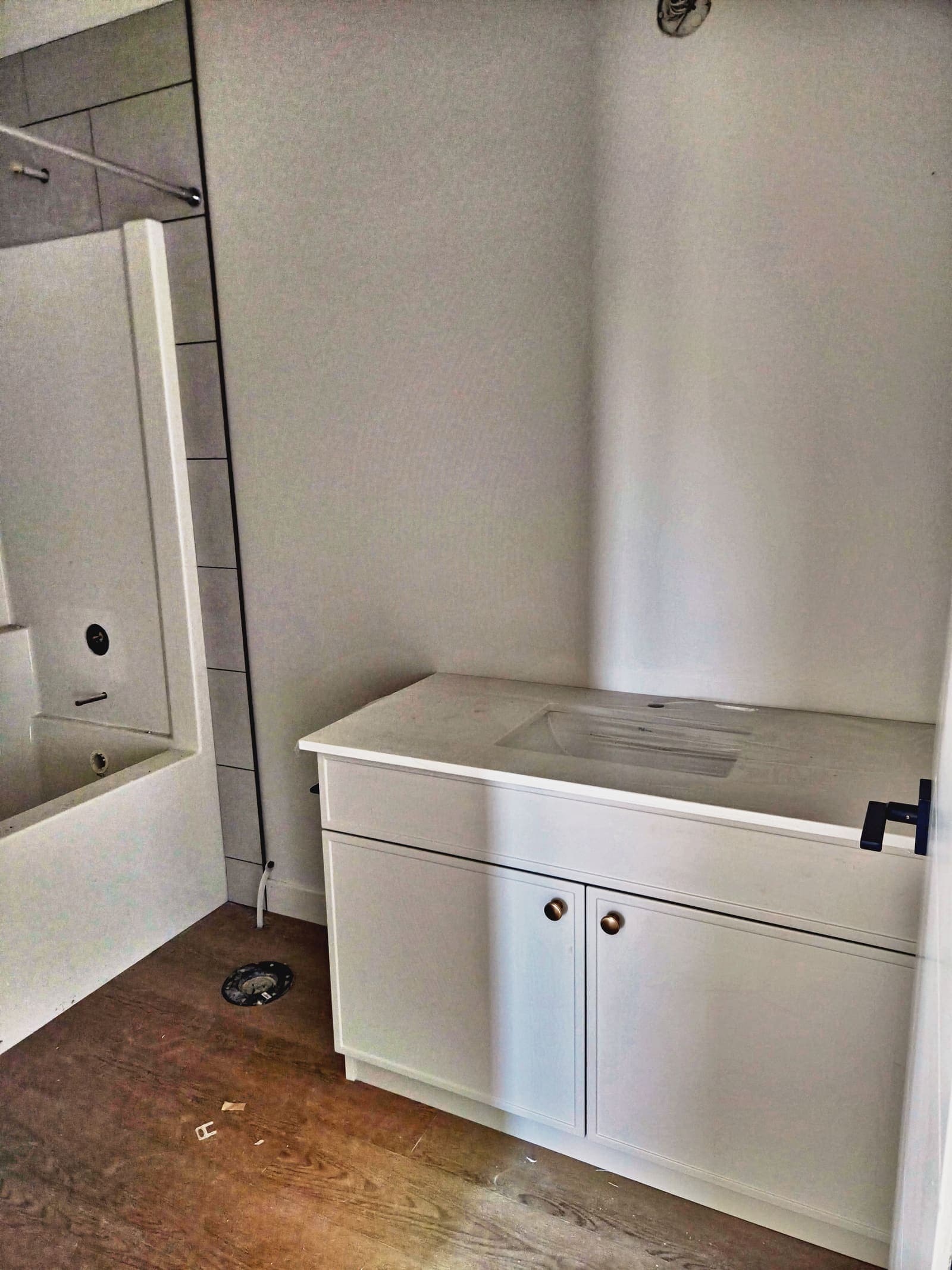 Upstairs bathroom with a white shaker vanity, brass knobs and a tub with tile surround